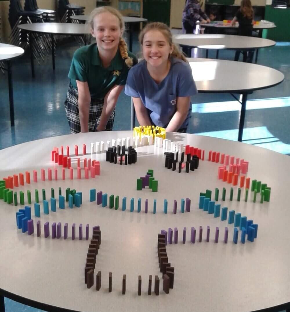 Two girls smiling at a table, showing off their tree built of dominoes
