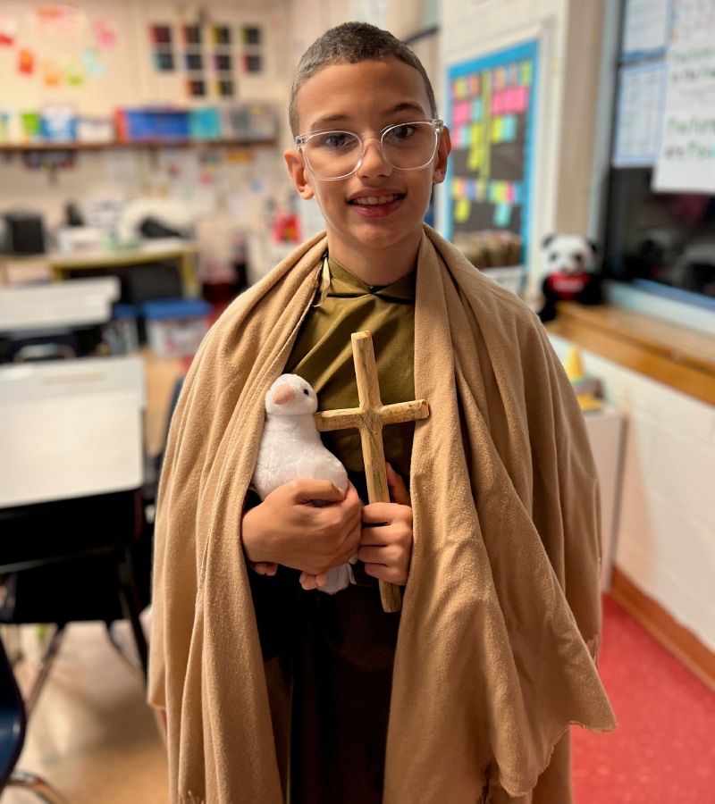 Student dressed up in a robe, holding a cross and a dove