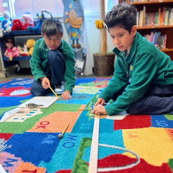 Two students solving a problem using a yard stick and some other tools